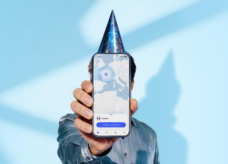Une personne portant un chapeau d’anniversaire et tenant un smartphone sur lequel s’affiche l’écran principal de l’application NordVPN.