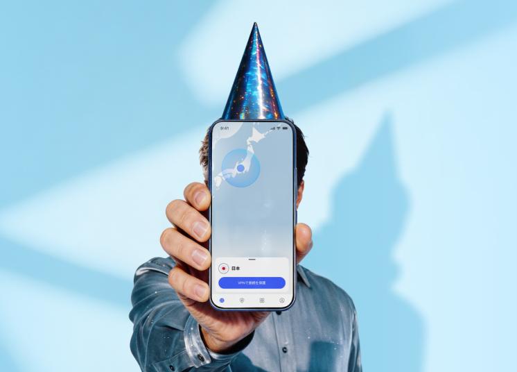 バースデーハットをかぶり、NordVPNアプリのメイン画面が表示されているスマートフォンを持っている人。