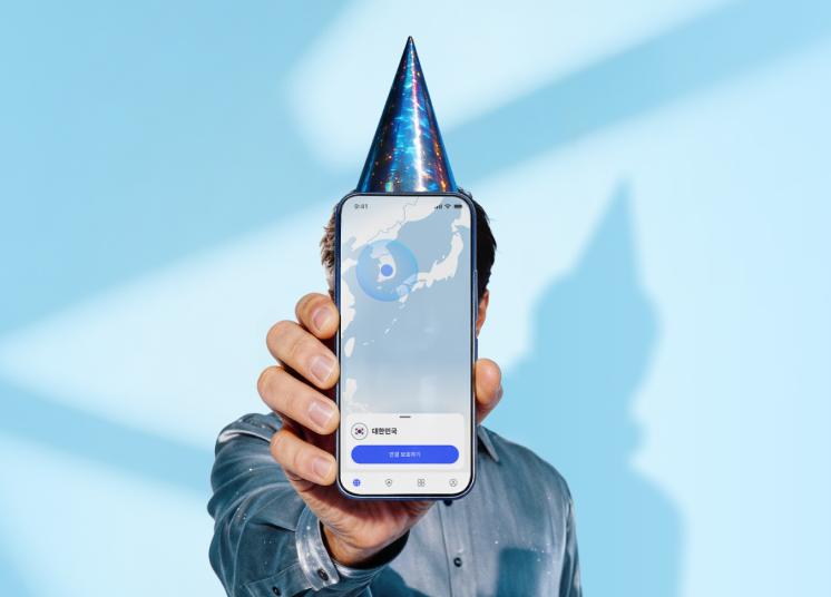 생일 모자를 쓴 사람이 NordVPN 앱의 메인 화면이 표시된 스마트폰을 들고 있는 모습