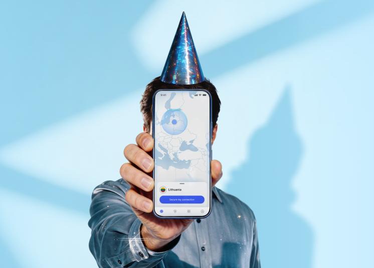 Žmogus su gimtadienio skrybėle laiko išmanųjį telefoną, kuriame matomas pagrindinis „NordVPN“ programėlės ekranas.