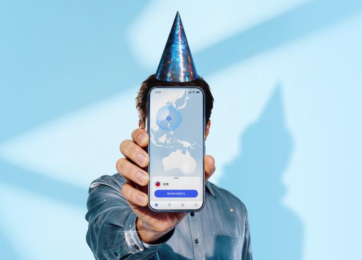 一個戴著生日帽的人拿著一部智慧型手機，螢幕上顯示著 NordVPN 應用程式的主介面。