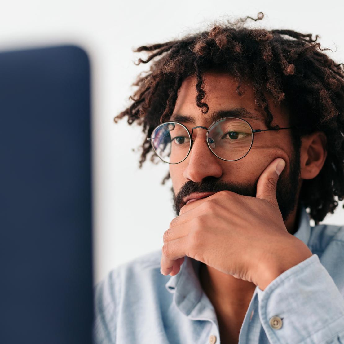 A person in glasses reading intently at a computer screen.