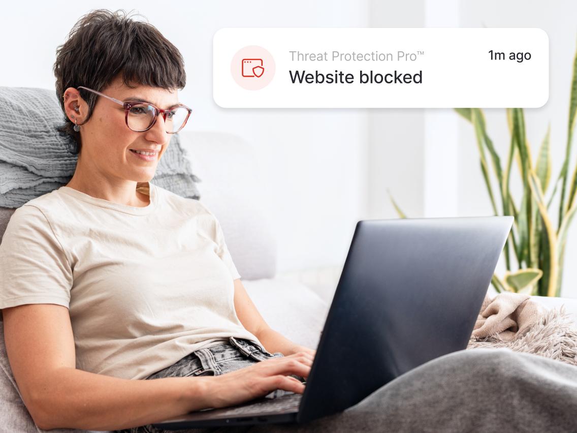 A laptop user sees a NordVPN alert showing a harmful site being blocked.