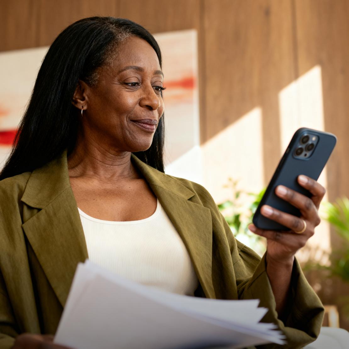 A woman checks her phone while reviewing documents related to home title insurance coverage.
