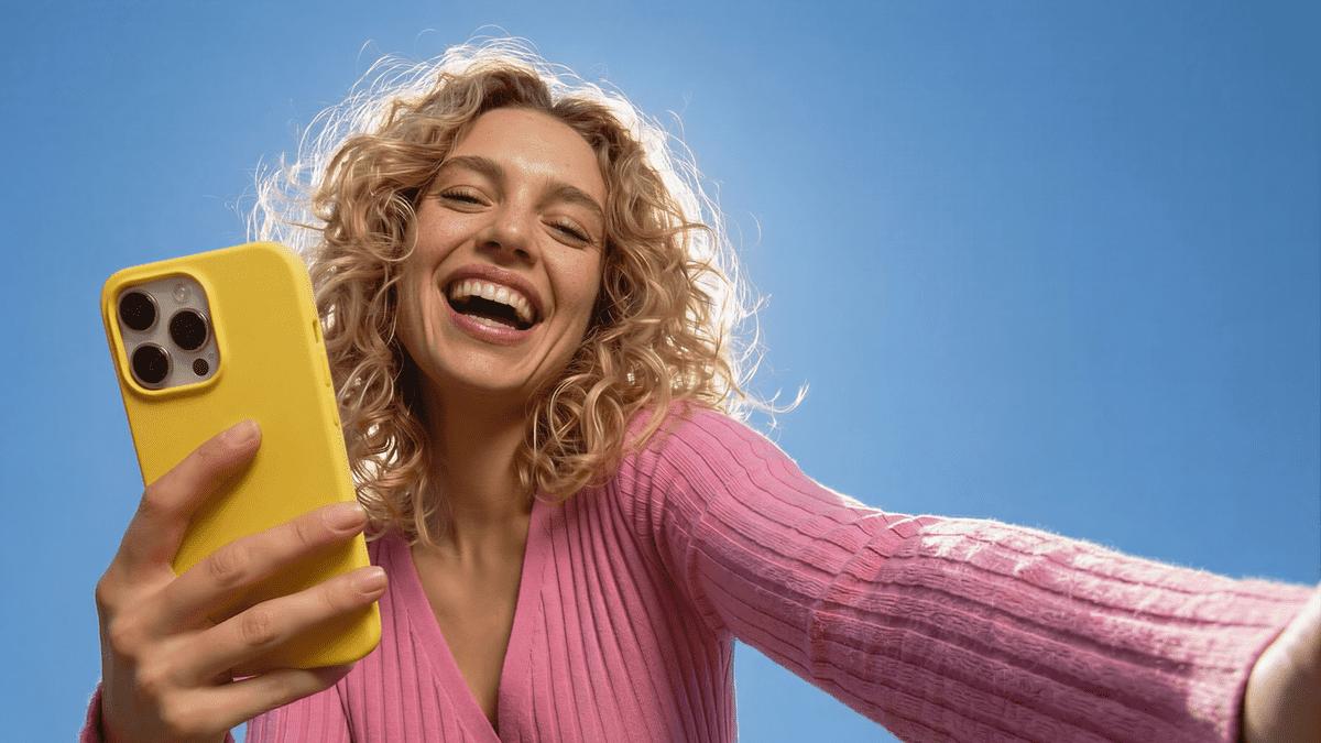 Woman taking a selfie with a yellow phone against a blue sky.