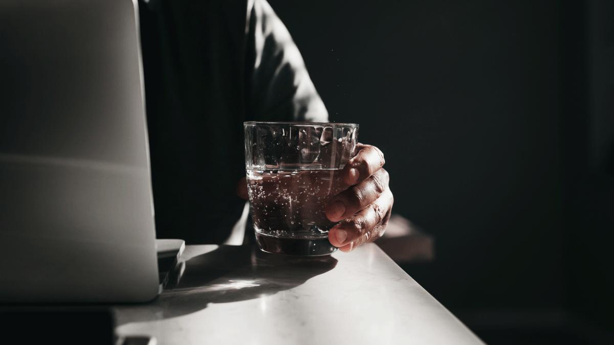 A persons hand holding a glass of water in front of a laptop.