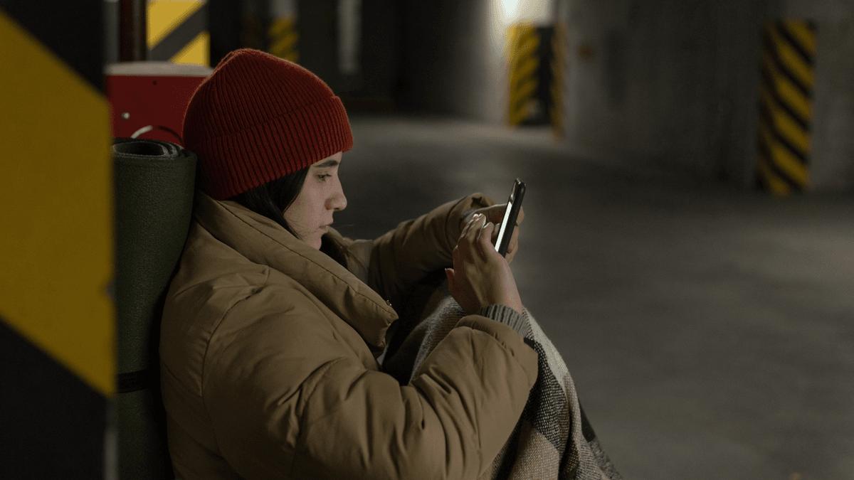 Person in a winter coat using a phone in an underground shelter.
