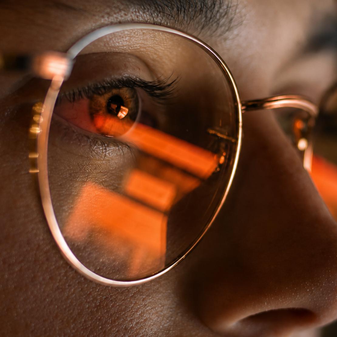 A close-up of a person with a compromised device screen reflecting on their glasses.