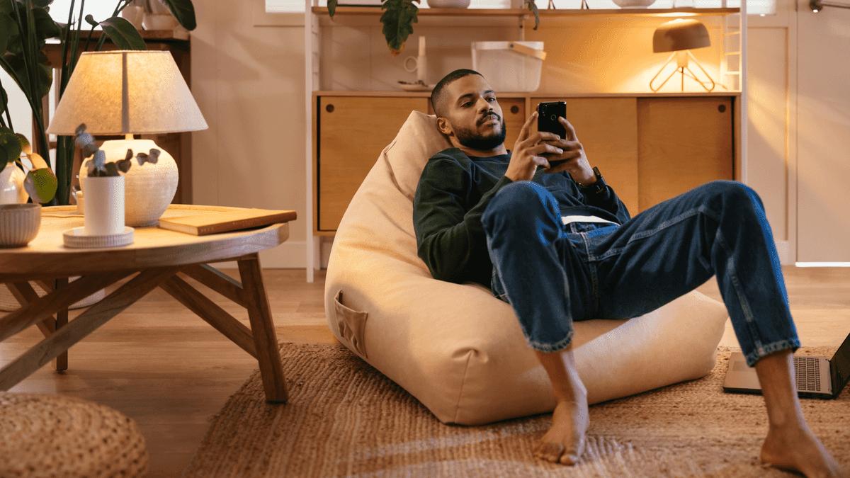 Man using his phone on a beanbag in a living room.