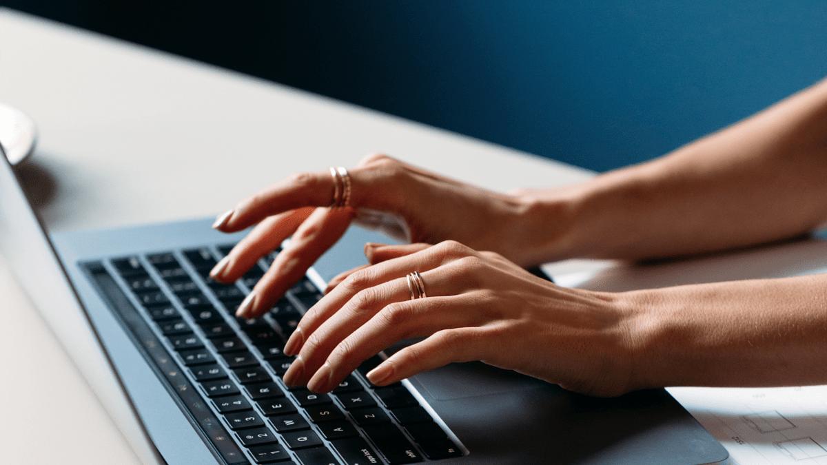 Hands typing on a laptop keyboard at a desk.