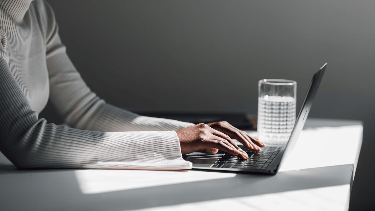 Woman typing on a laptop at a sunlit desk.