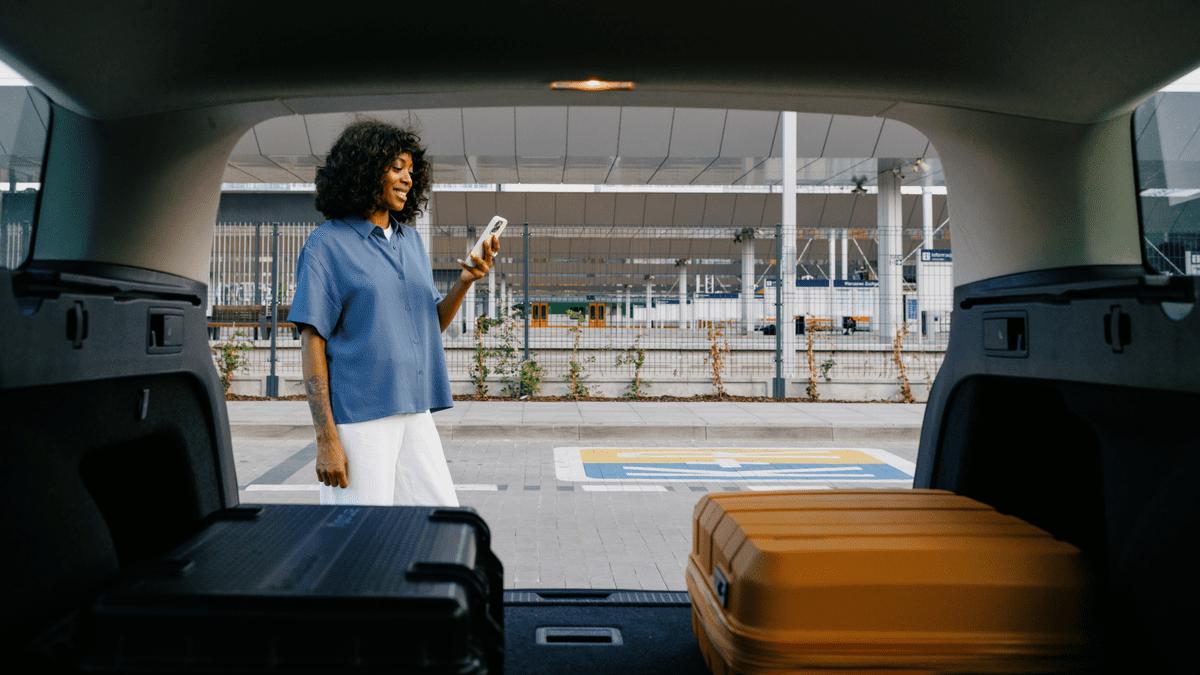 Woman using her phone beside an open car boot with suitcases.