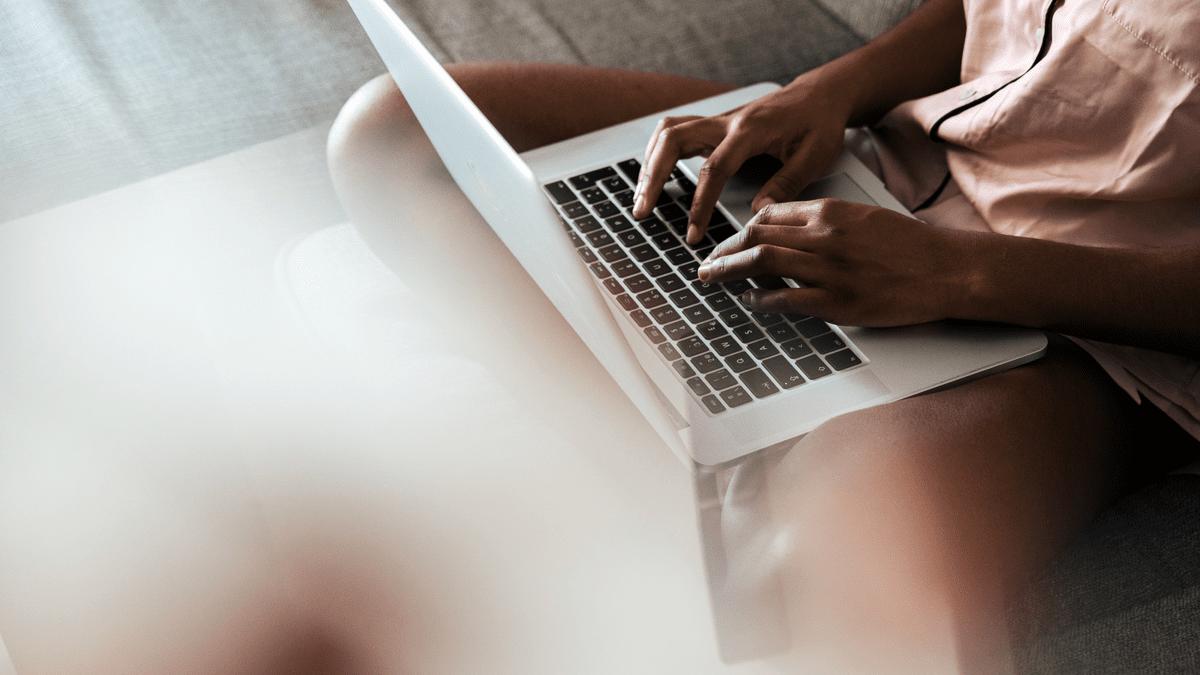 Person typing on a laptop while sitting on a sofa.