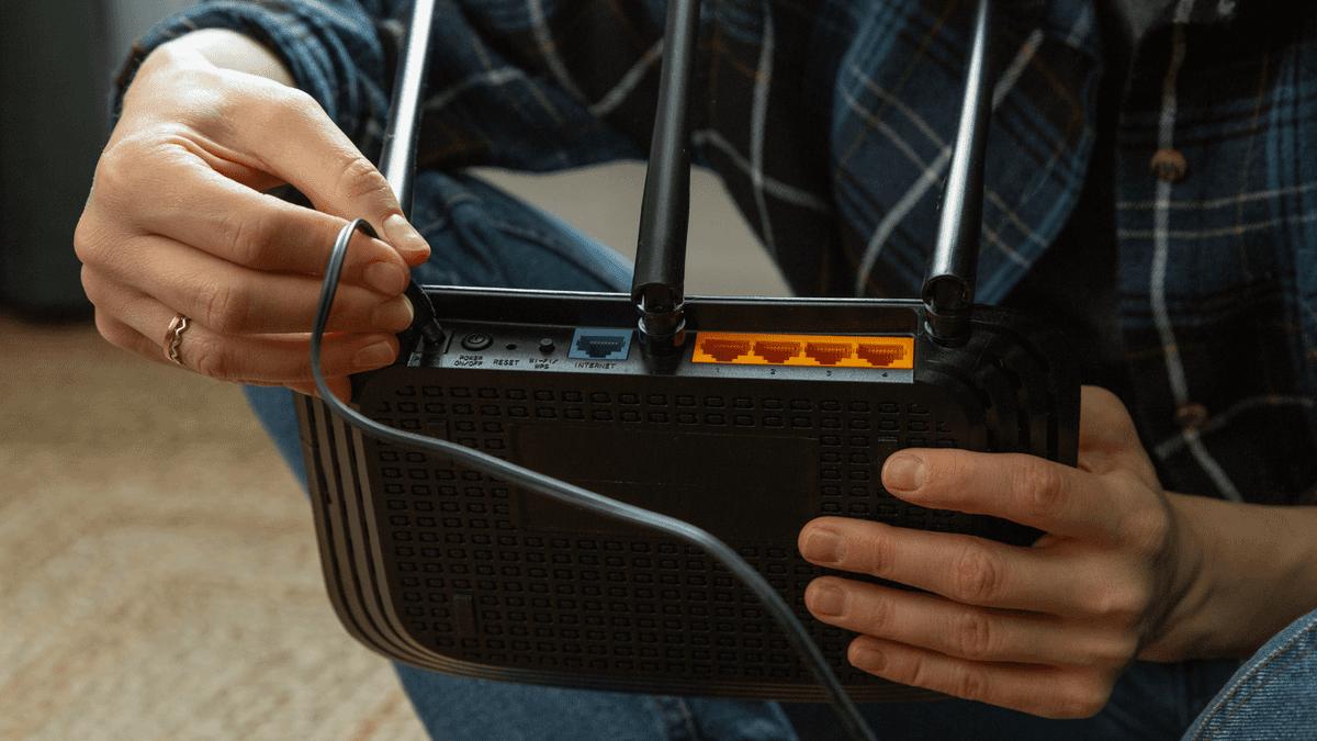 Hands connecting a cable to the back of a Wi-Fi router.
