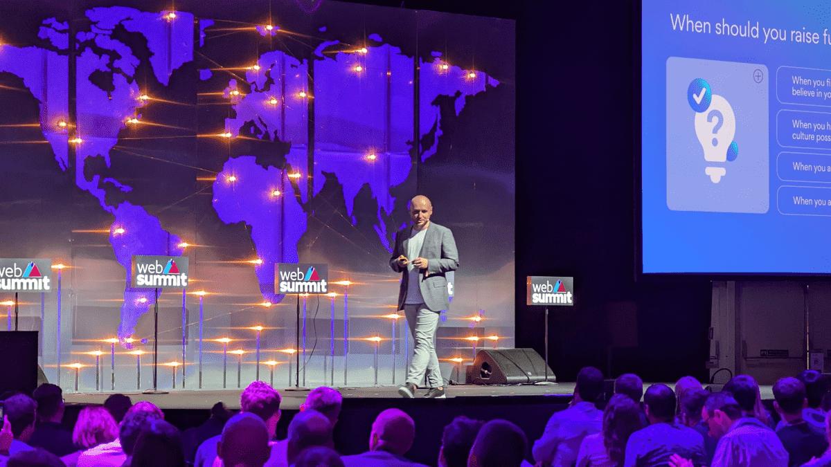 Tom Okman on stage at Web Summit 2022 in front of a world map and a funding slide.