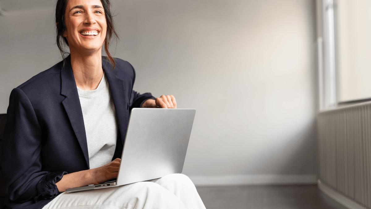 Woman smiling while using a laptop on her lap.