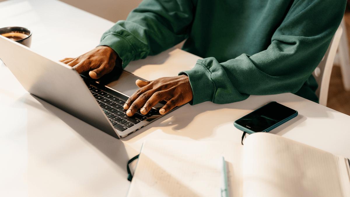 Developer typing on a laptop beside a phone and notebook.
