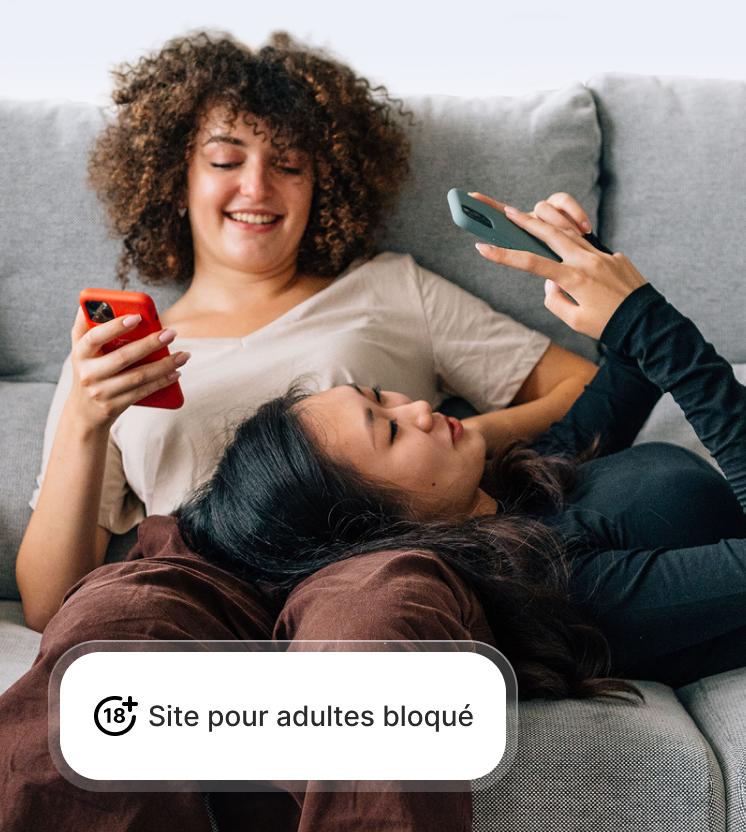 Deux femmes utilisant leur téléphone en toute sécurité grâce à la protection contre les arnaques et le phishing qui bloque les sites pour adultes.