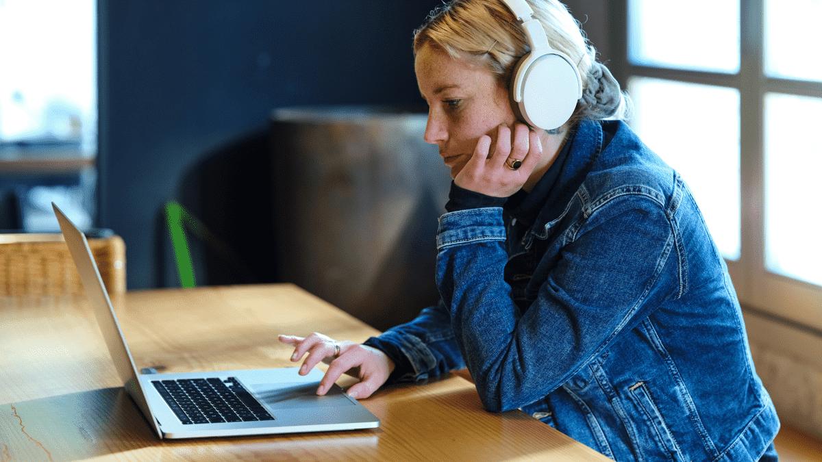 Woman with headphones using a laptop at a wooden table.