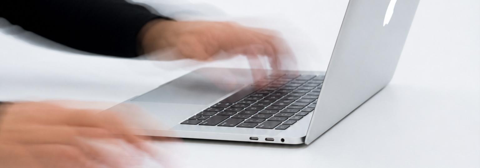 Hands typing quickly on a laptop keyboard.