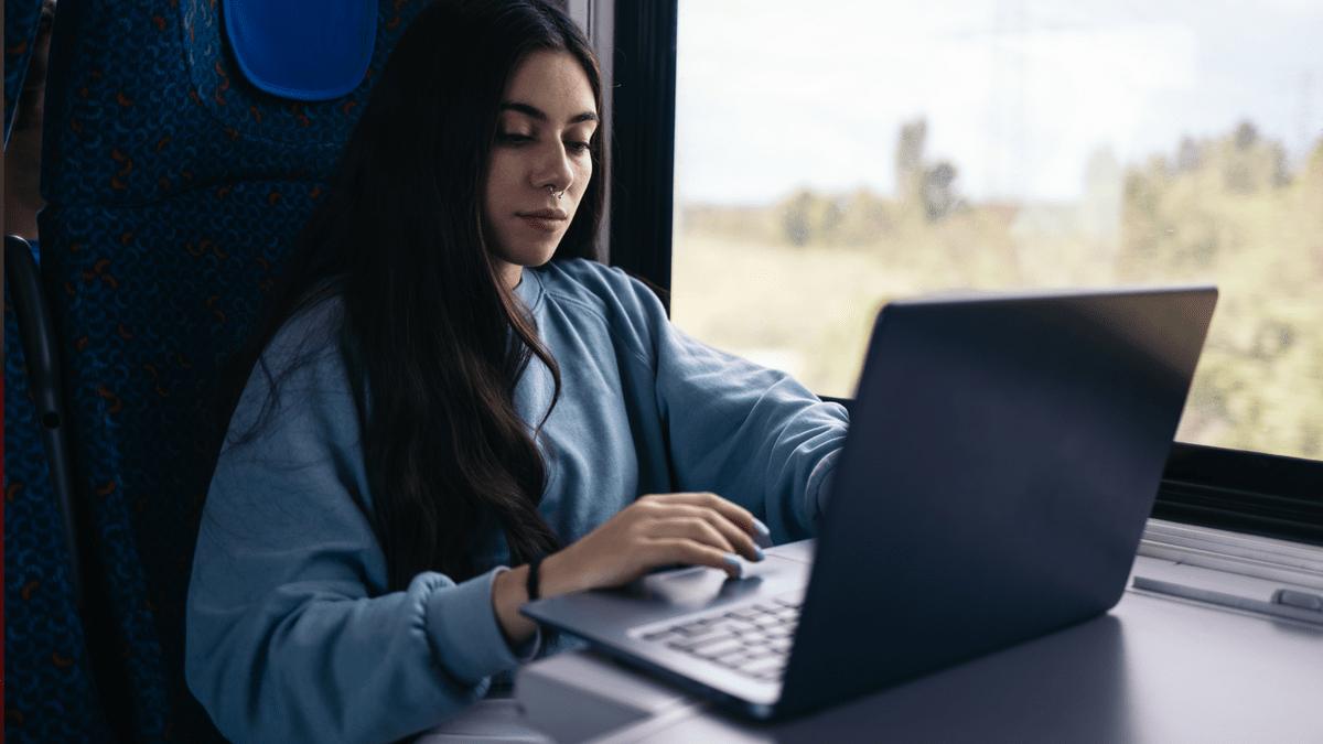 Woman using a laptop on a train beside the window.
