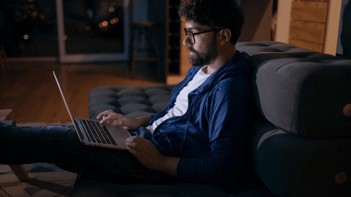 Man using a laptop on a sofa at night.