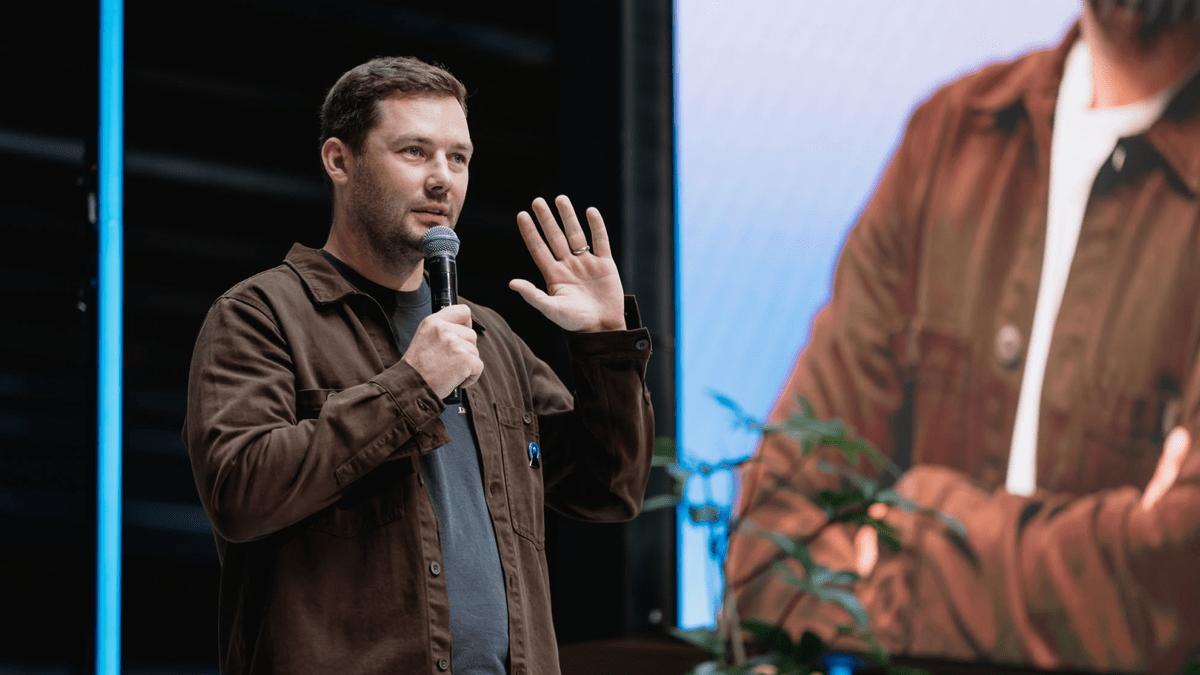 Domininkas Virbickas, Product Director at NordVPN, presenting on stage with his talk projected on the screen behind him.