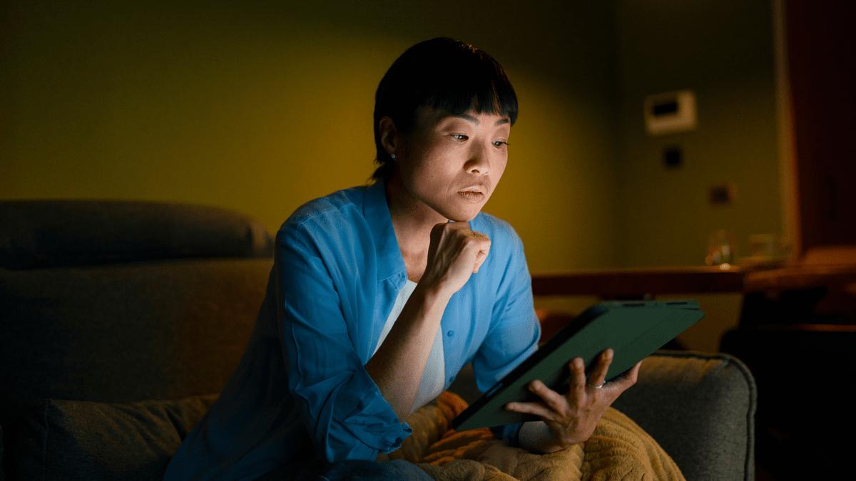 Woman looking at a tablet on a sofa at night.