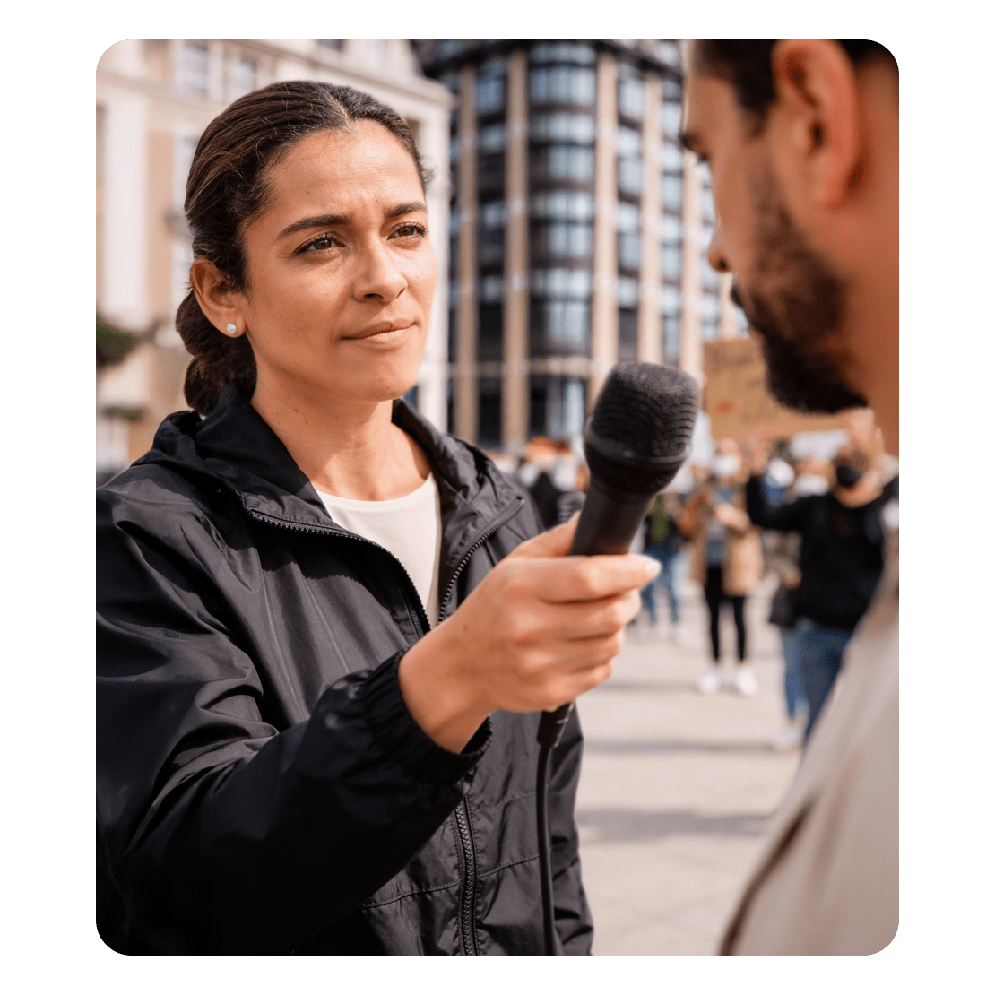 En journalist holder en mikrofon, mens han interviewer en mand ved en offentlig demonstration.