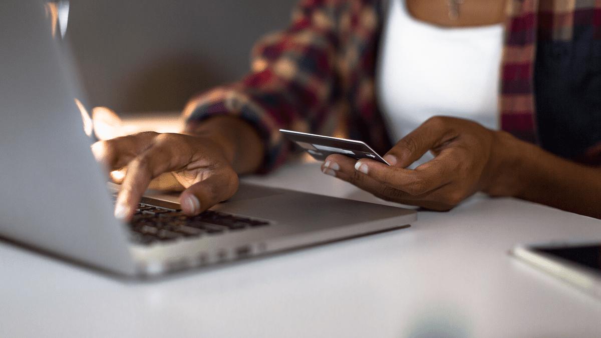 Hands holding a bank card while typing on a laptop.