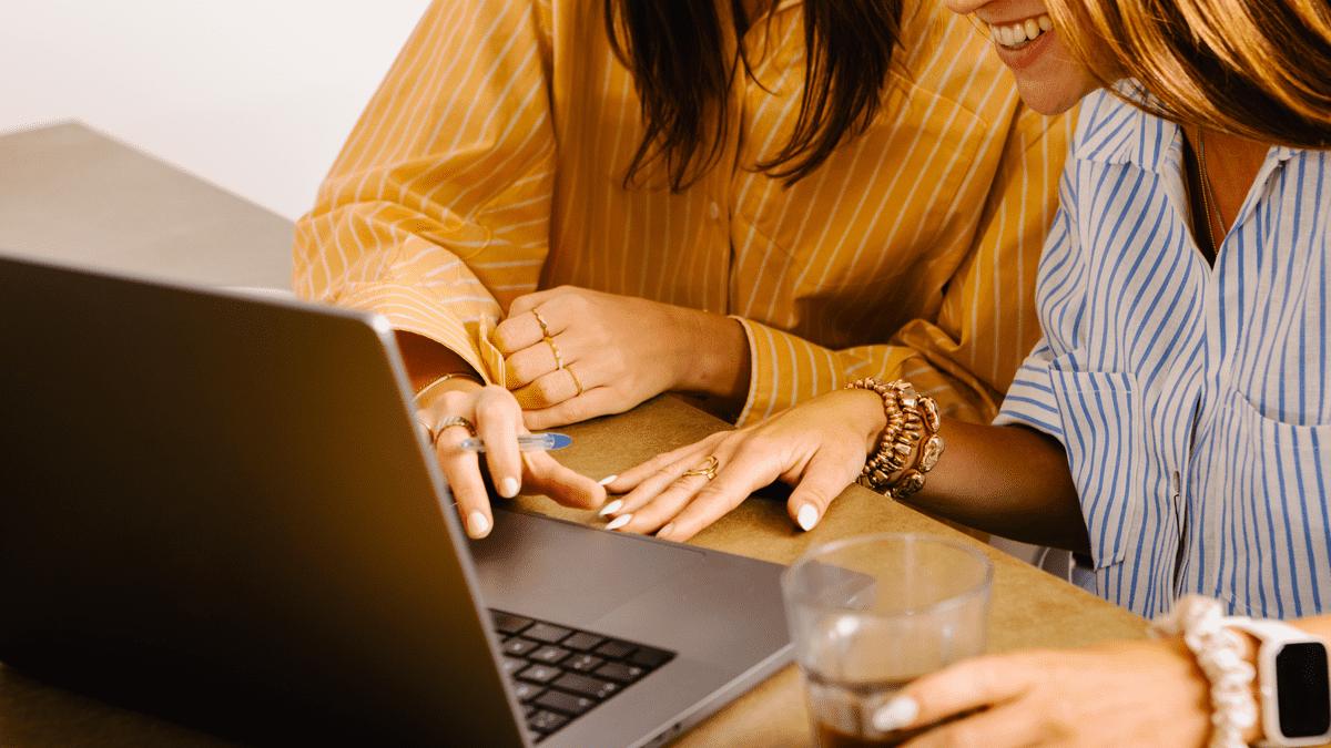 Two colleagues laughing while working at a laptop.