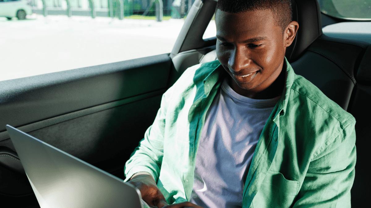 Man using a laptop in the back seat of a car.